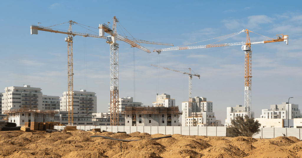 בניין מגורים רב קומות בשלבי בנייה מתקדמים עם מנופים על רקע שמיים כחולים.