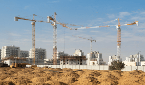 בניין מגורים רב קומות בשלבי בנייה מתקדמים עם מנופים על רקע שמיים כחולים.