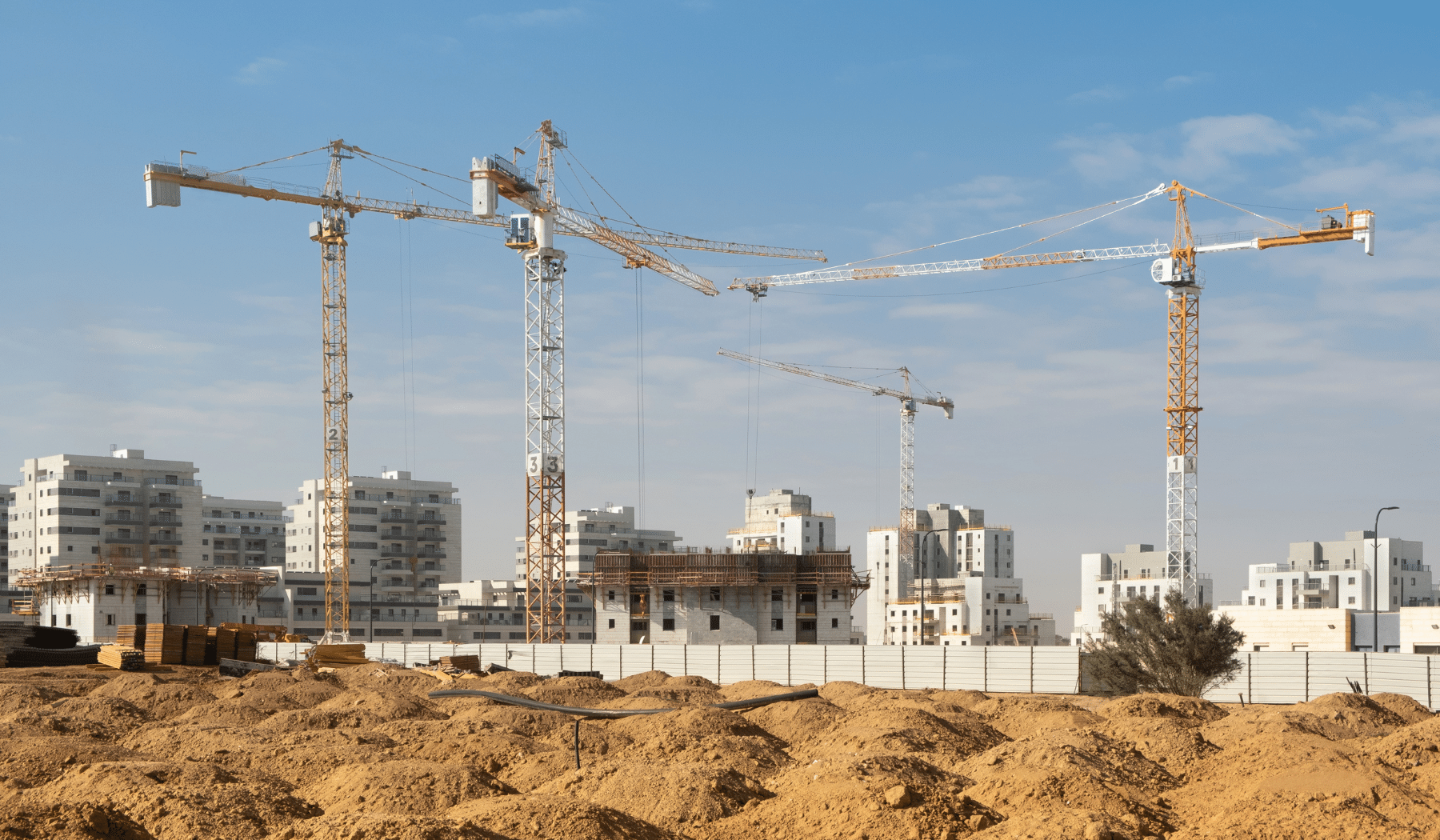 בניין מגורים רב קומות בשלבי בנייה מתקדמים עם מנופים על רקע שמיים כחולים.